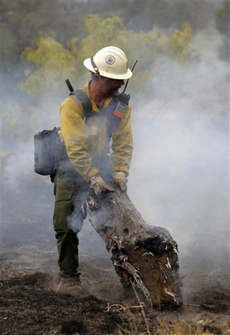 Firefighter Ron Riise, from the U.S. Forest Service in California, pulls a burning stump to a safer spot north of Ranger, Texas, as wildfires continue to burn west of Fort Worth.